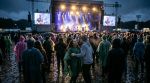 Crowd watching a live band on stage during a rainy outdoor concert